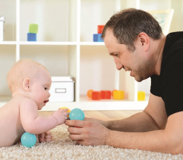 Papá y bebé mirándose, jugando con sonajas sobre la alfombra