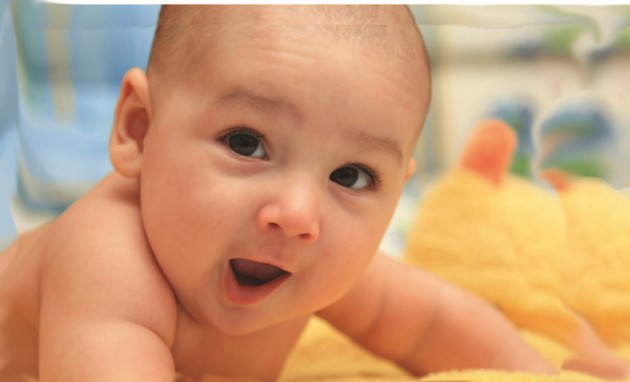 Bebé sobre su barriga apoyado sobre sus codos fijando su mirada en alguien, con su boquita abierta