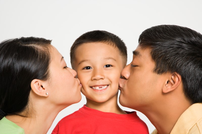Two parents kiss their son on the cheek