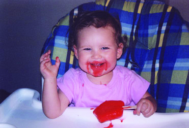 Smiling baby eating a popsicle in their high chair