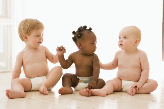Tres bebés sentados se miran uno al otro mientras dos sostienen sus manos y uno le toca la espalda a la bebé a su lado