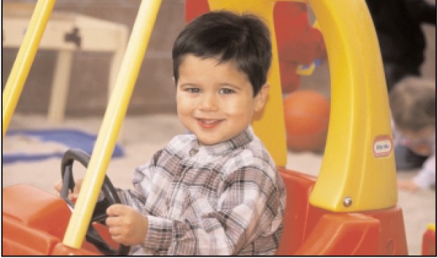 Niño pequeño sonriente al volante de un carrito amarillo de plástico