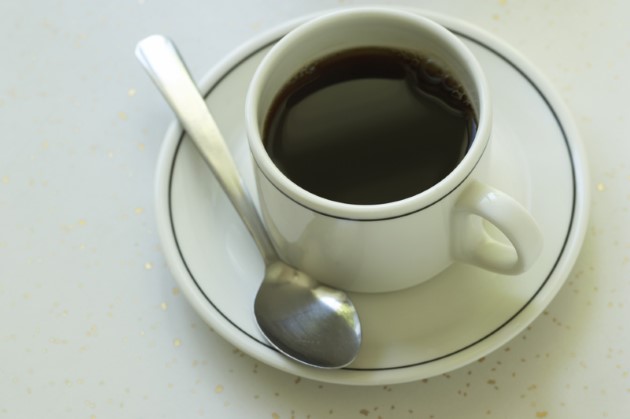 Una tacita de café negro sobre su plato y cucharilla