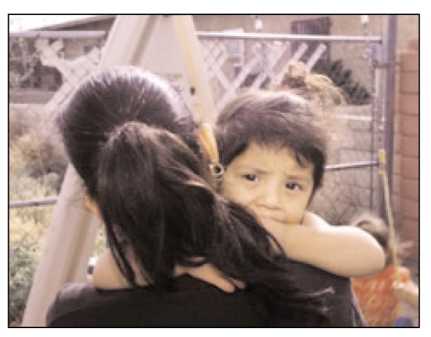 Niño pequeño con mirada seria y una mano en su boca mientras su mamá le carga en sus brazos