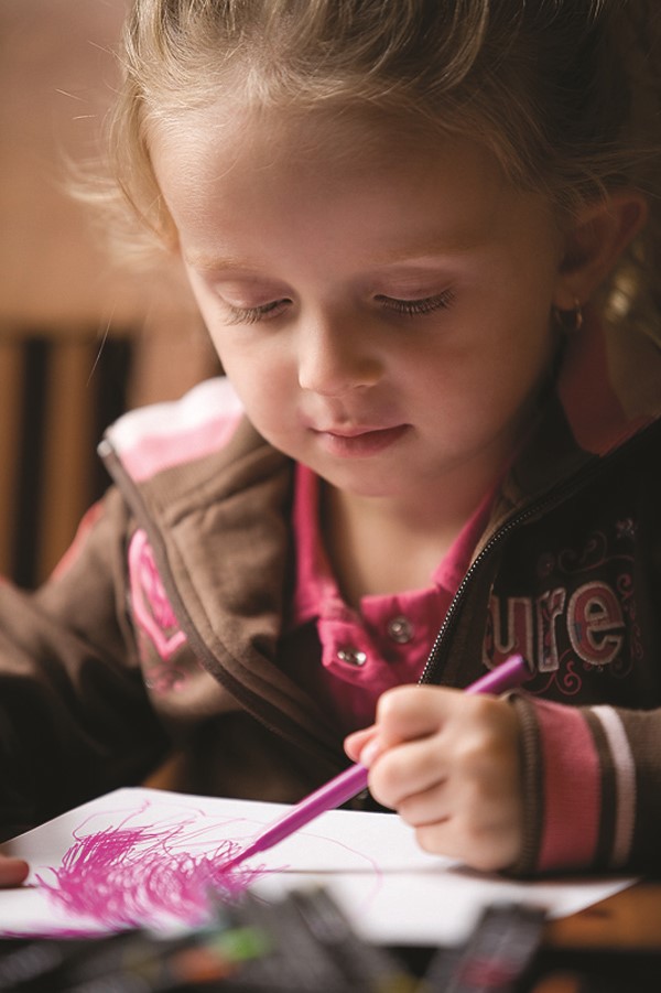 Niña pequeña pintando trazos color fuchsia en un papel con su mano izquierda