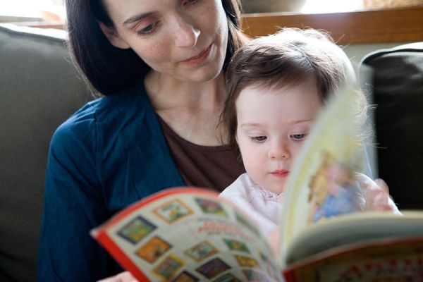 Niña lee un libro atentamente sentada con su mama