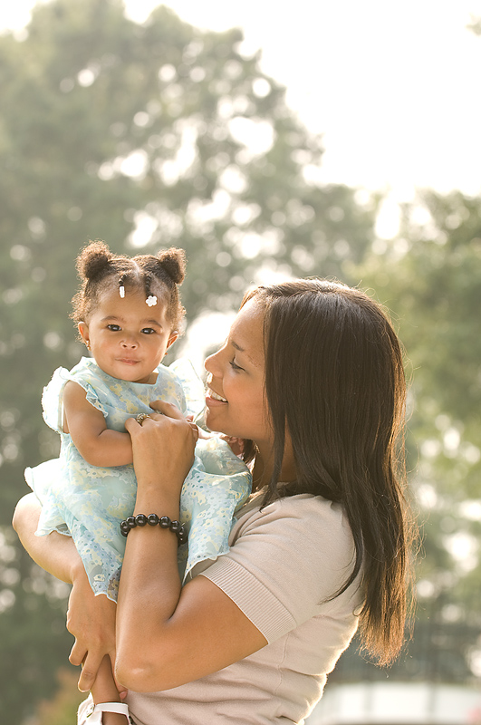 Mamá observa y sonríe a su bebé sonriente mientras la carga sosteniendo una de sus manos
