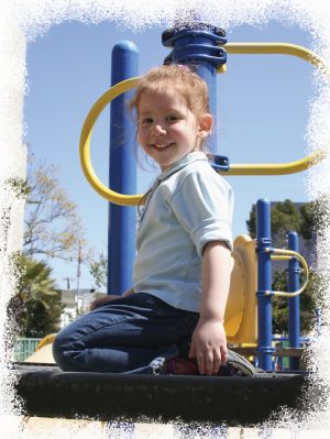 Niña pequeña sonriente arrodillada sobre una estructura de trepar en un parque infantil de juegos