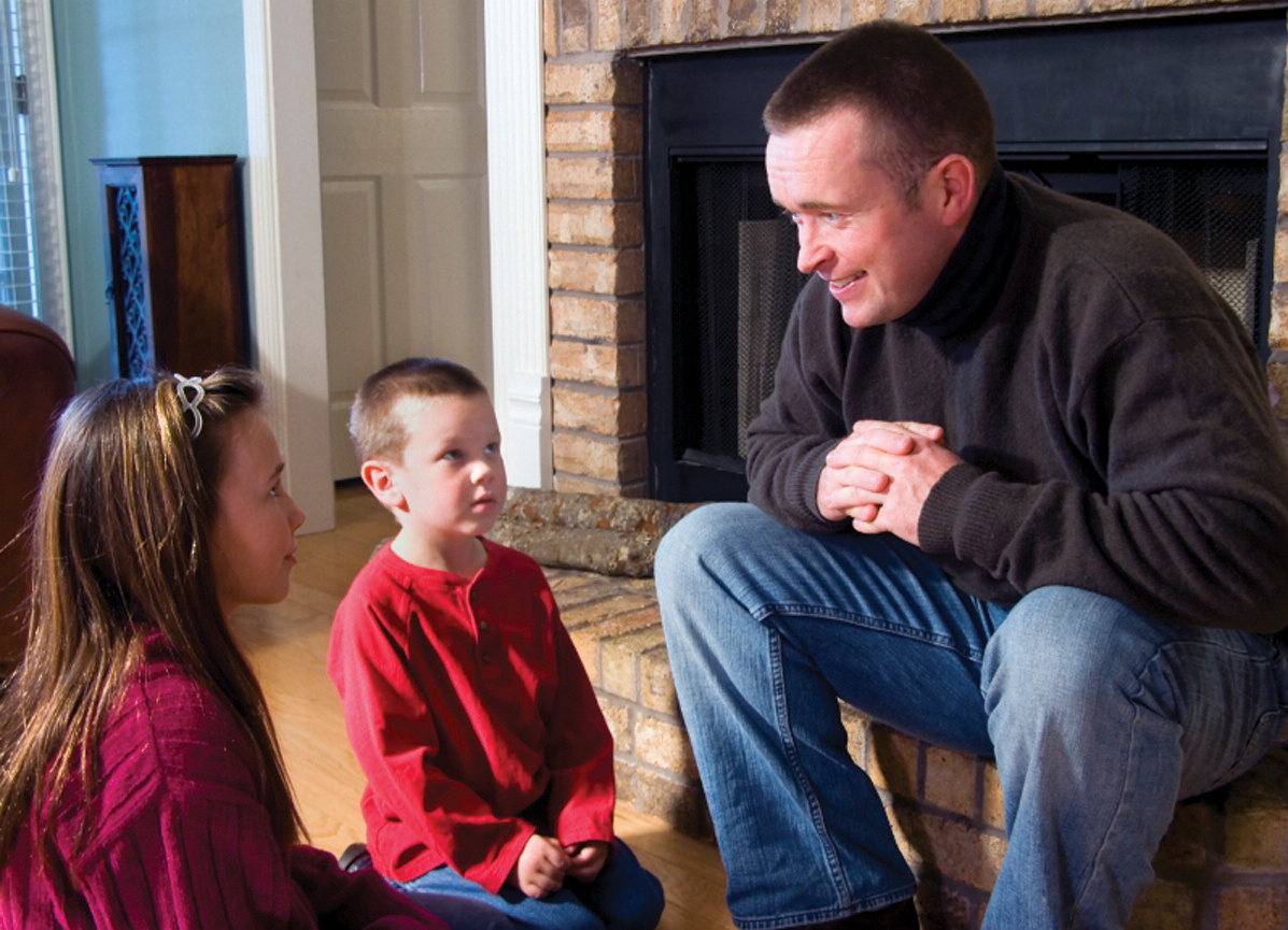 Papá conversando con tres niños pequeños sentados frente a una chimenea
