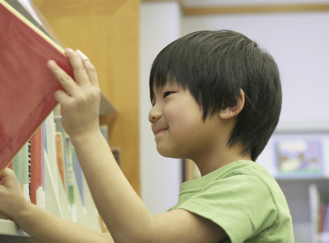Niño pequeño toma un libro rojo de un estante de libros con ambas manos