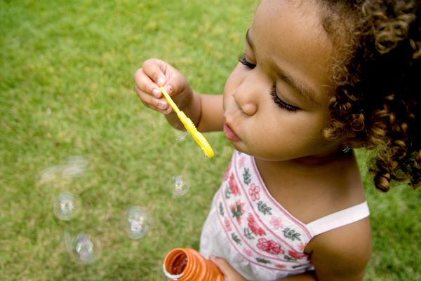 Niña sosteniendo un potecito en su mano soplando burbujas/pompas de jabón