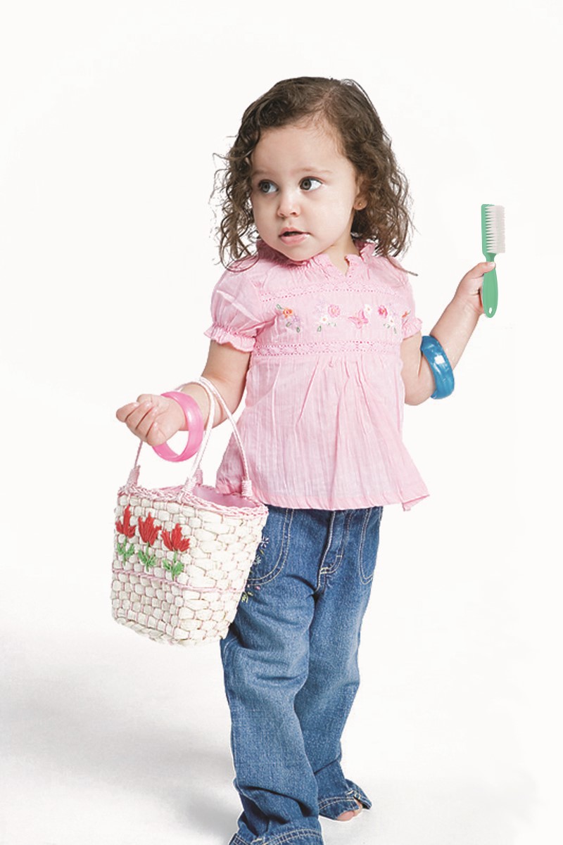 Niña pequeña mira con atención mientras sostiene en una mano un cepillo para el cabello y en la otra un bolso