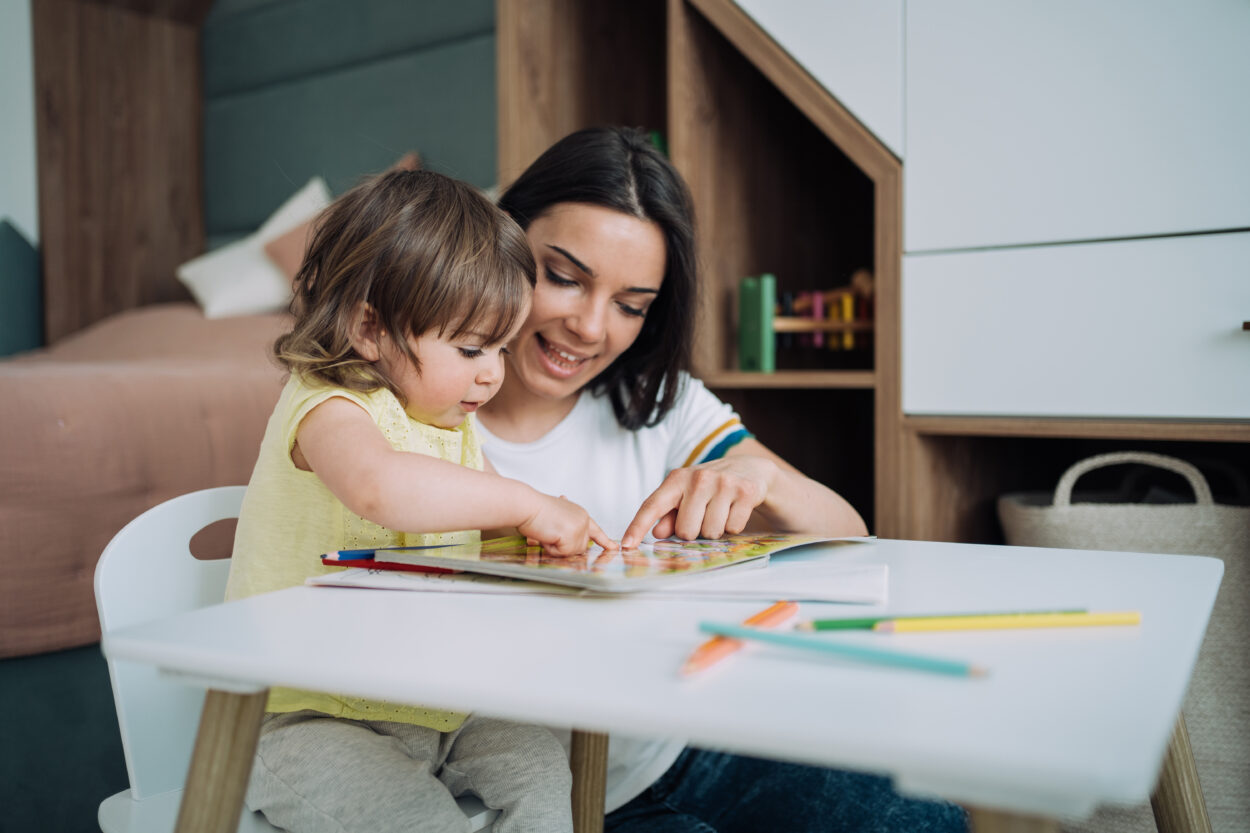 Mamá y su hija pequeña señalan con sus dedos a las imágenes de un libro
