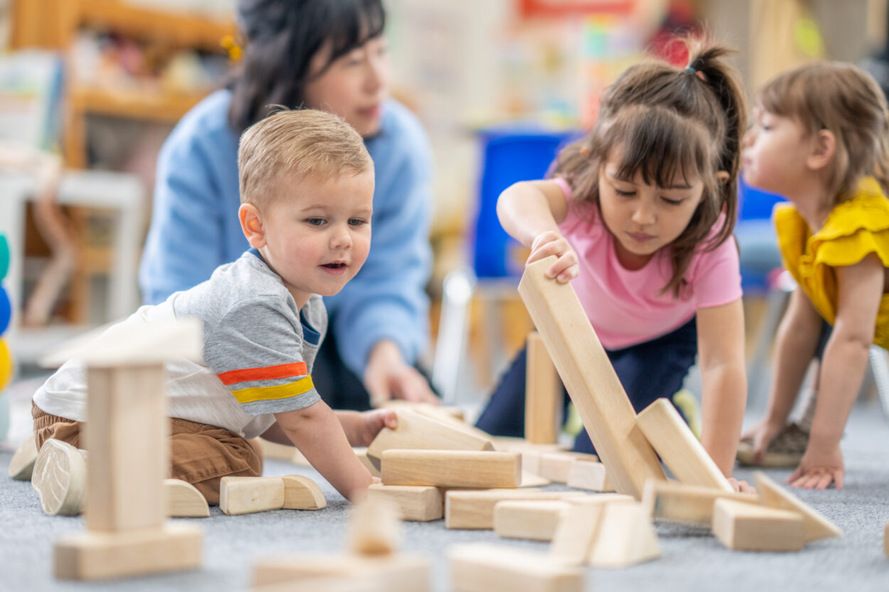 Un niño pequeña juega con bloques de madera con varios niños y  niñas en edad preescolar