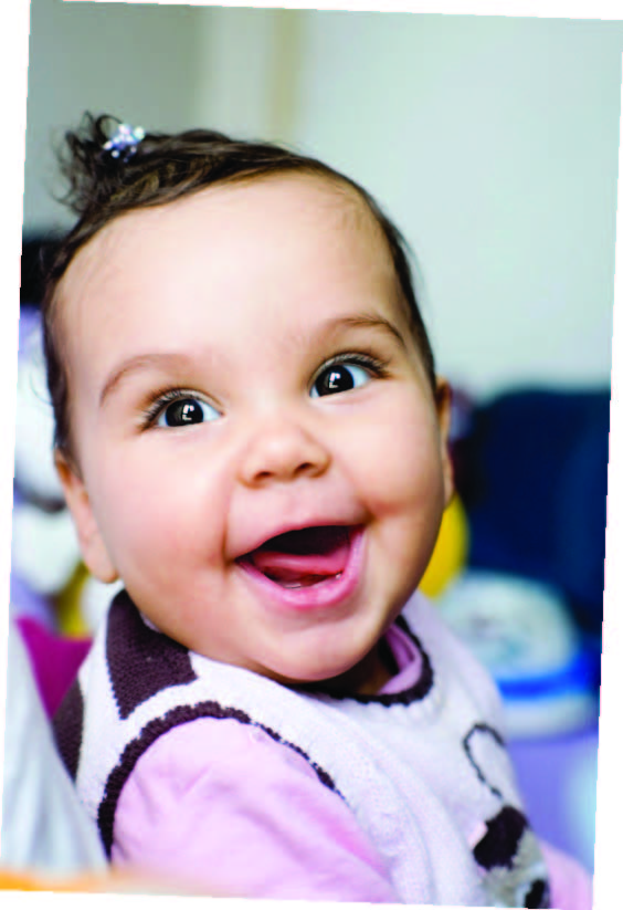 Bebé con ganchito en el cabello, sentada con apoyo, fijando su mirada y sonriendo