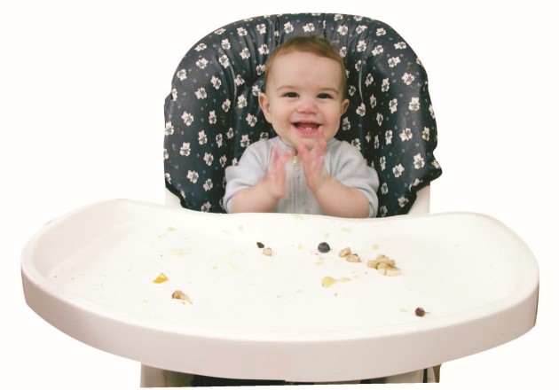 Niño pequeño sentado sobre su silla de comer con comida en trozos pequeños sobre el tope blanco