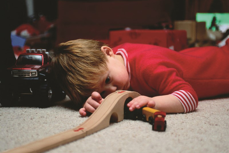 Niño pequeño observa recostado en el piso su tren y pista de tren