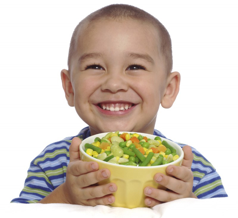 Niño pequeño sonríe mientras sostiene un bol con vegetales