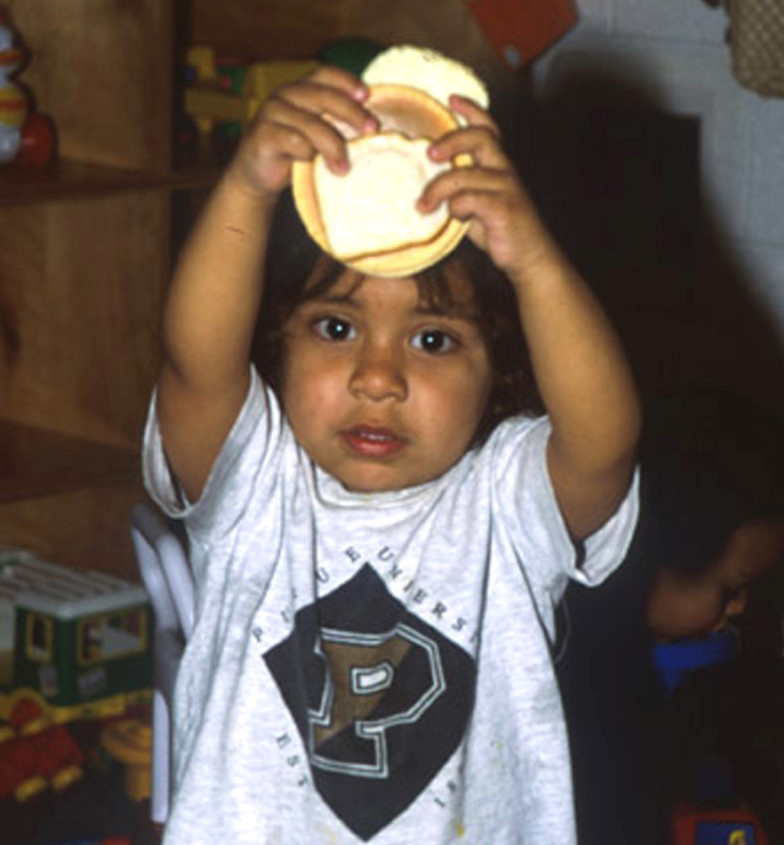 Niño pequeño alza y sostiene algo para comer sobre su cabeza