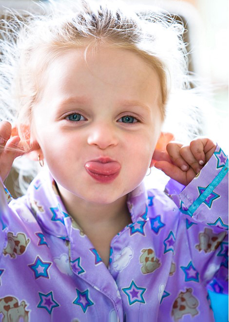 Niña pequeña halando sus orejas y sacando su lengua con expresión sonriente