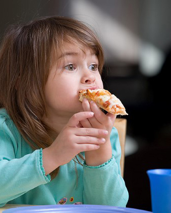 Niña pequeña mordiendo una rebanada de pizza sosteniéndola con sus manos