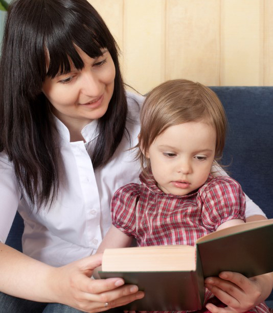 Mamá carga a su hija pequeña mientras leen un libro