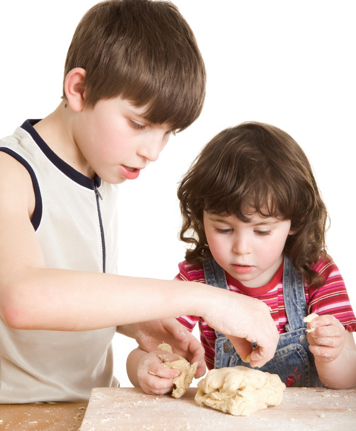 Dos niños manipulan masa para comer, el niño mayor sosteniendo la mano de la niña menor