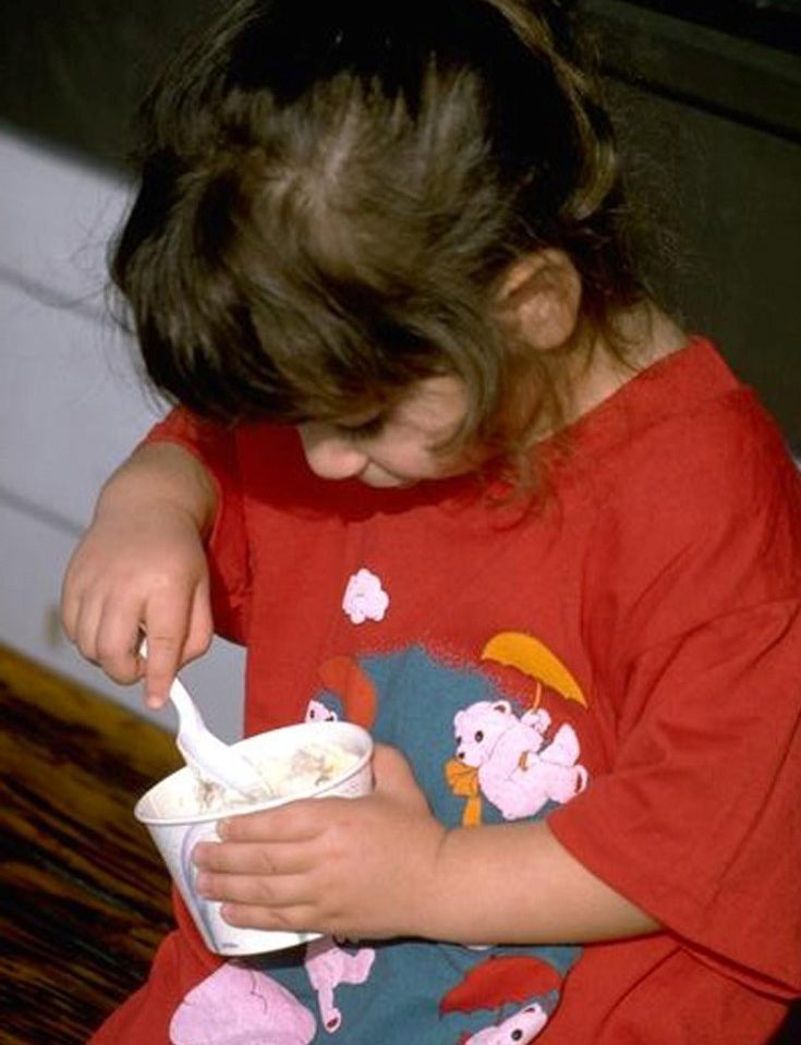 Niña pequeña utiliza una cucharita mientras come helado de un recipiente en sus piernas