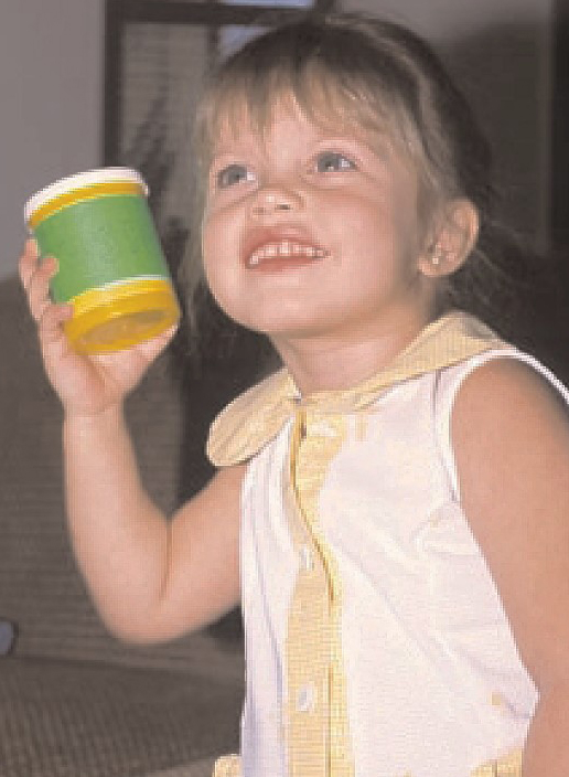 Niña pequeña sonriente sostiene muestra un tarro/frasco plástico amarillo con tapa