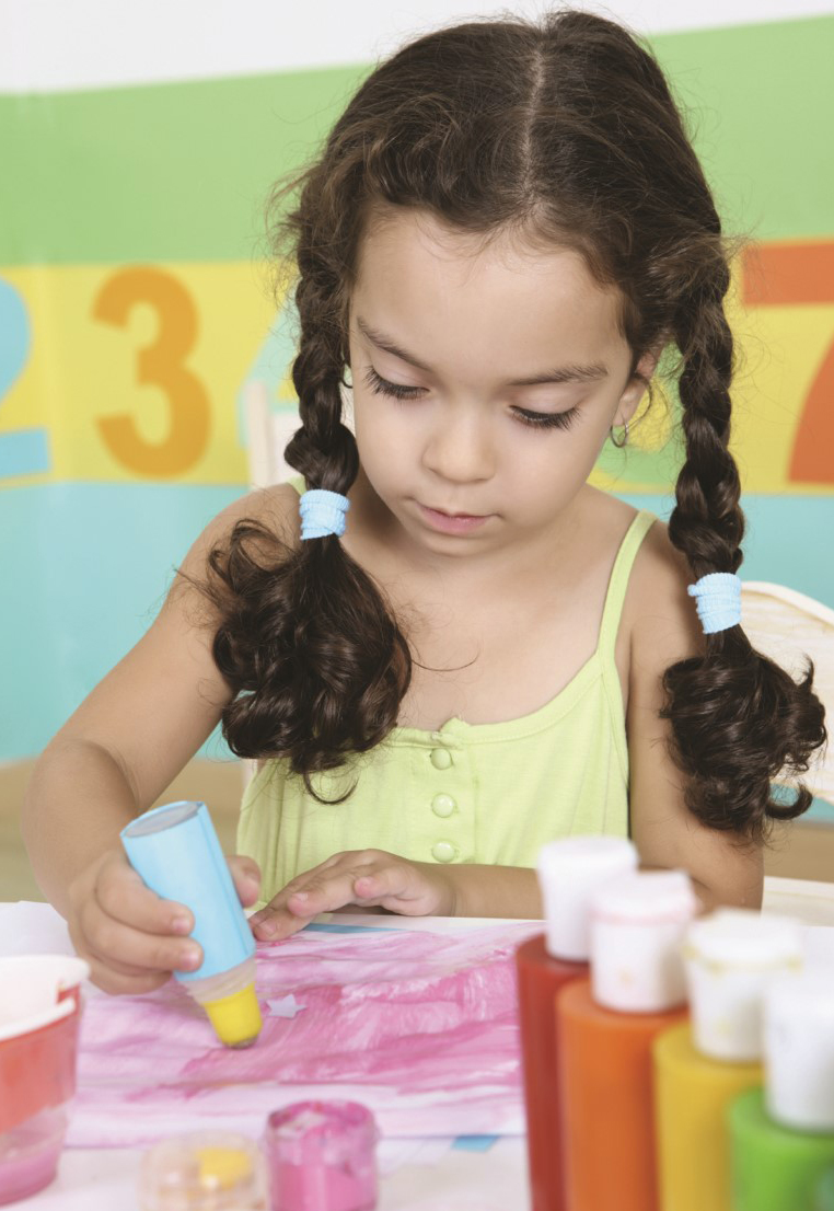 Niña pequeña presiona un estampador de pintura amarilla sobre un papel de colores