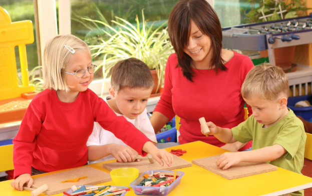 Educadora juega con tres niños/niñas utilizando piezas de madera de colores sobre tableros en una guardería/jardín de infancia