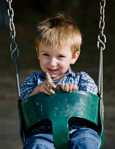 Niño pequeño sonríe sentado en columpio para infantes