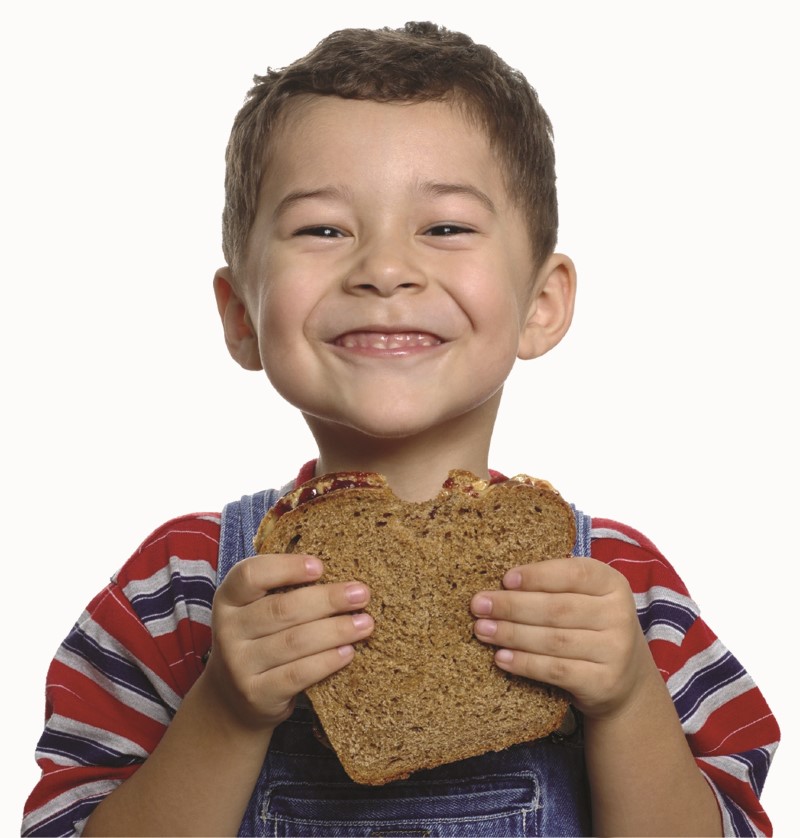 Niño pequeño sonriente sostiene con sus manos un emparedado/sánduche de pan integral