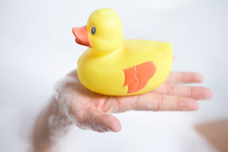 Una mano llena de espuma para baño sostiene a un patito de goma amarillo