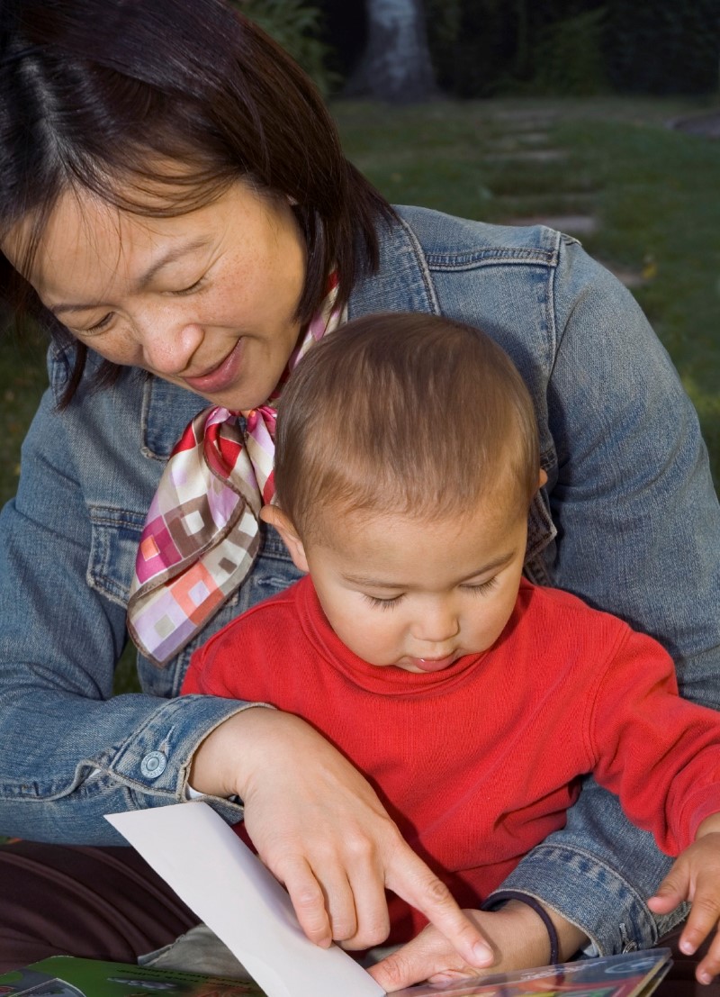 Niño pequeño lee atentamente un libro con su mamá o cuidadora
