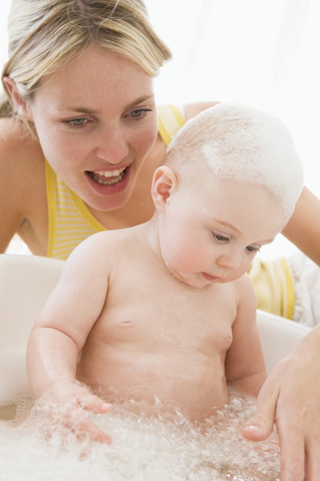 Mamá y bebé tocan la espuma del jabón durante el baño del bebe en la tina/bañera