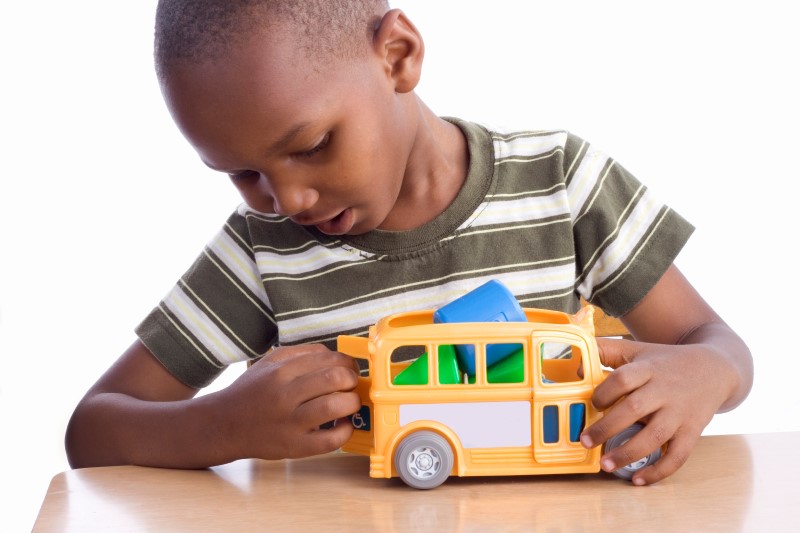 Niño pequeño inserta formas de plástico en un bus amarillo de juguete