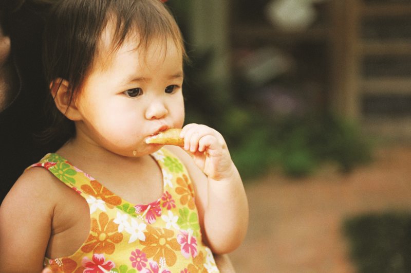 Niña pequeña come un pedazo de comida con su mano