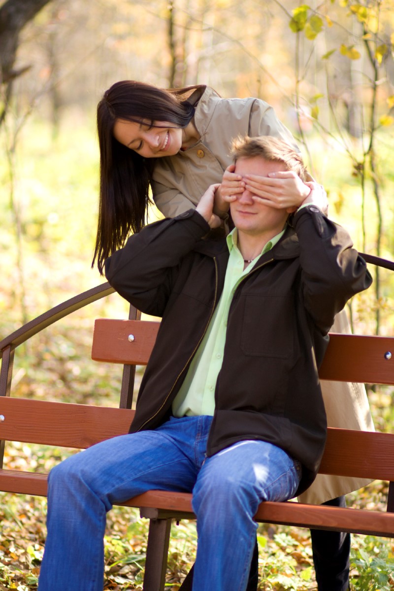 Mamá le cubre los ojos a su pareja sentados en un banco en un parque