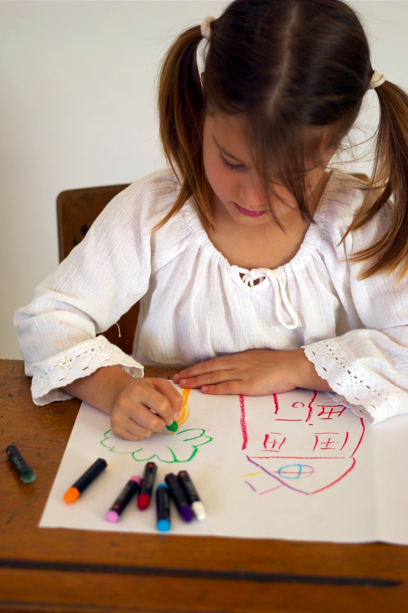 Niña pequeña dibuja usando marcadores de colores sentada frente a un escritorio
