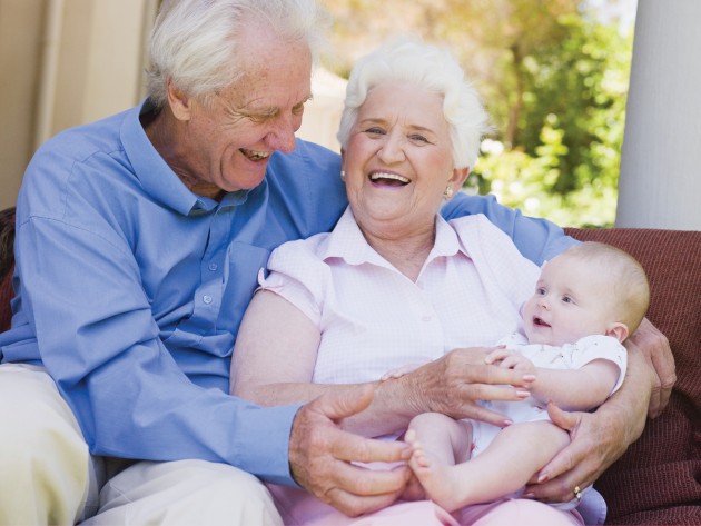 Bebé fija su mirada en su abuelo mientras abuelo y abuela sonríen, cargado en brazos de la abuela