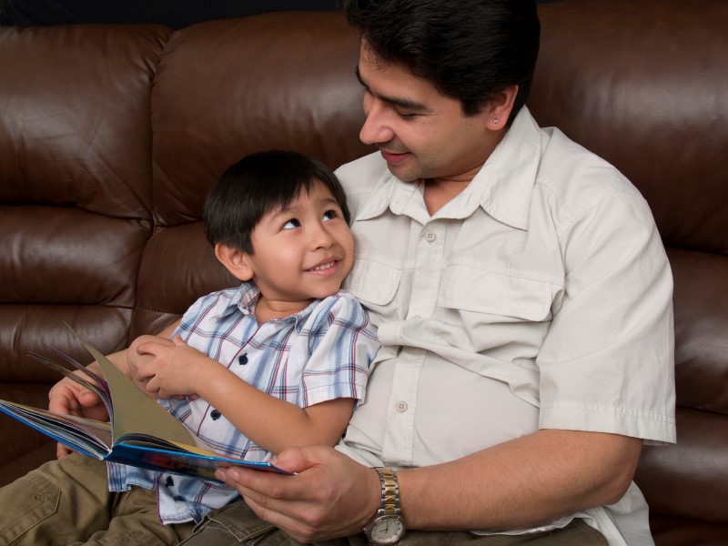 Papá e hijo leen un libro sentados en un sofá y se miran sonrientes