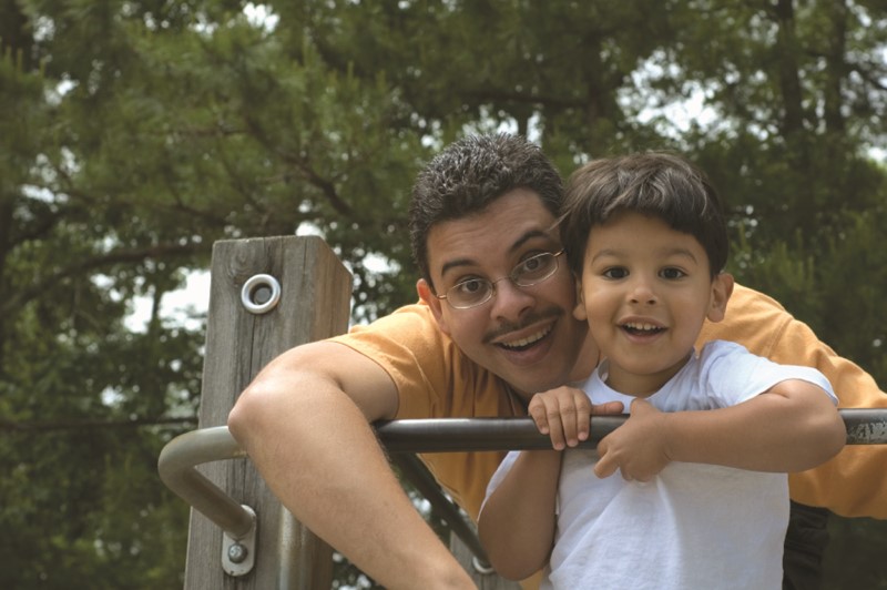Papá e hijo pequeño sonríen sobre una estructura para trepar en un parque de juegos infantiles