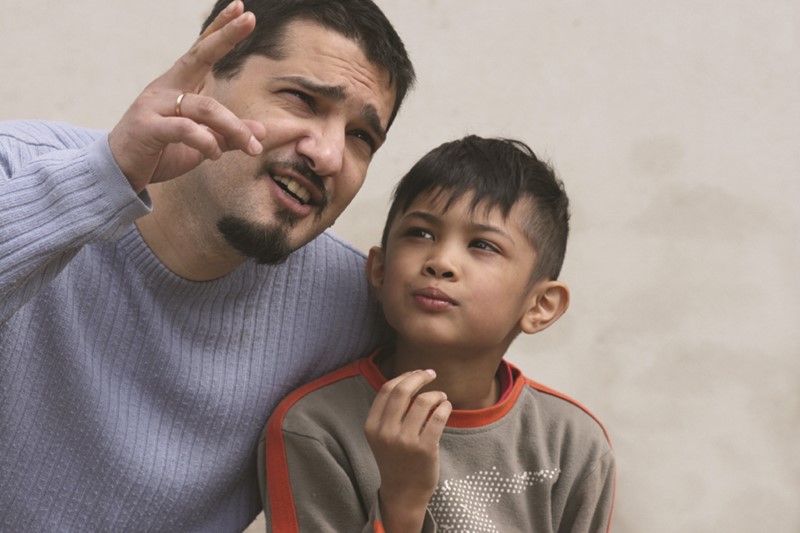 Papá muestra algo con sus dedos a su hijo quien le observa mientras conversan