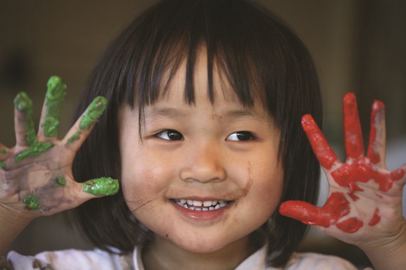 Niña pequeña muestra sus dedos con estampas de pintura digital rojo y verde mientras sonríe