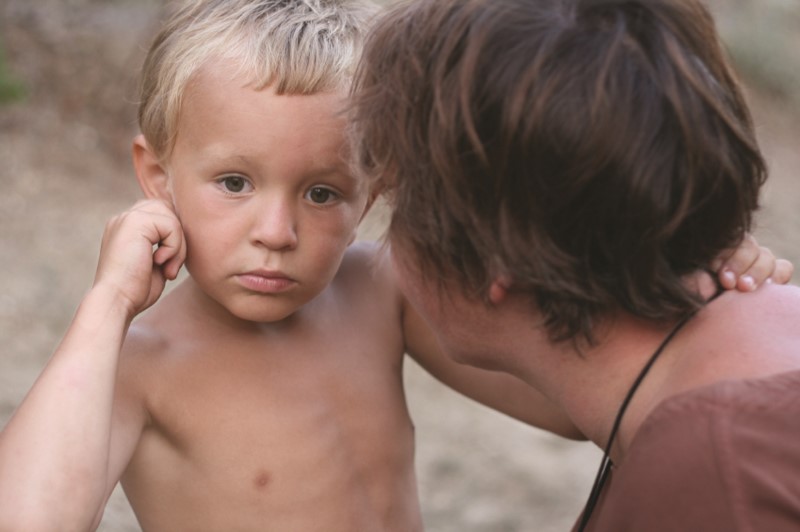 Niño pequeño en un espacio de playa/arena presta atención a su mamá quien le habla muy de cerca