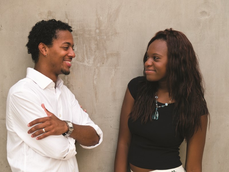 Pareja sonriente apoyados contra una pared viéndose a los ojos