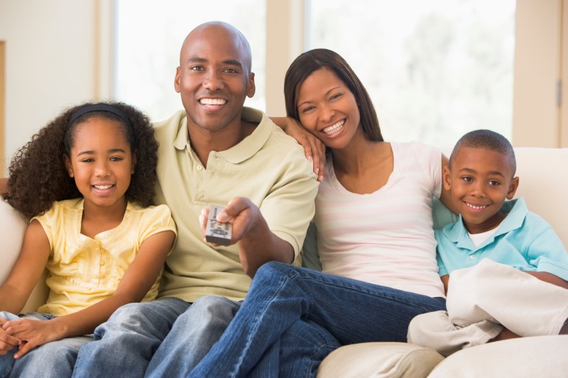 Familia de papá y mamá, hijo pequeño e hija mayor viendo un programa en la televisión