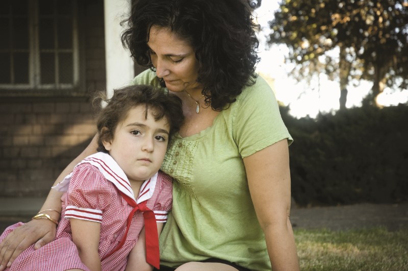 Mamá abraza a su niña pequeña con expresión triste mientras se sientan en el césped/grama