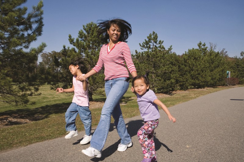 Mamá caminando con dos niñas pequeñas saltando en un espacio abierto